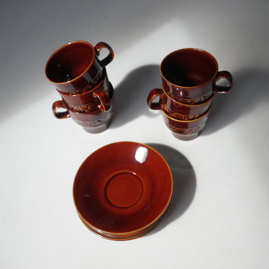 Three pairs of glossy reddish-brown ceramic cups with handles and matching saucers, arranged on a white surface with strong directional shadows.