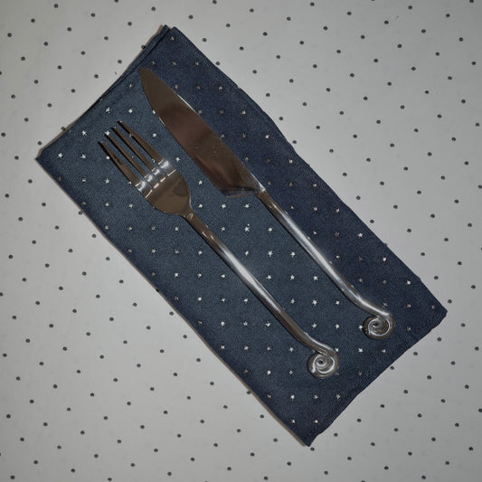 Denim napkins with silver stars on a polka dot table cloth with spiral cutlery on top.