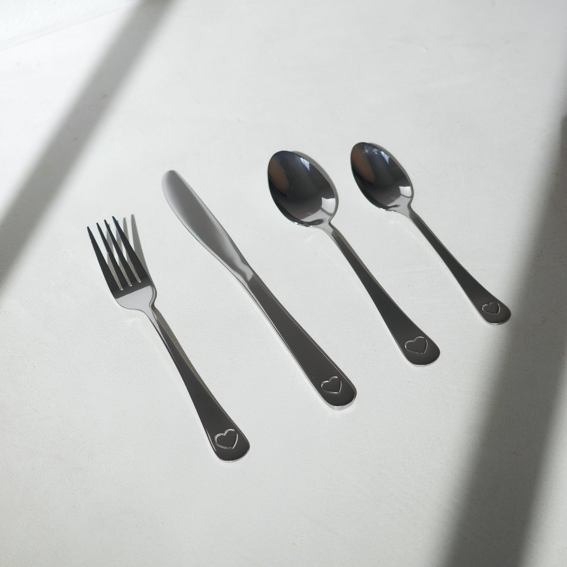 Set of silver cutlery with heart-shaped designs on a light gray background
