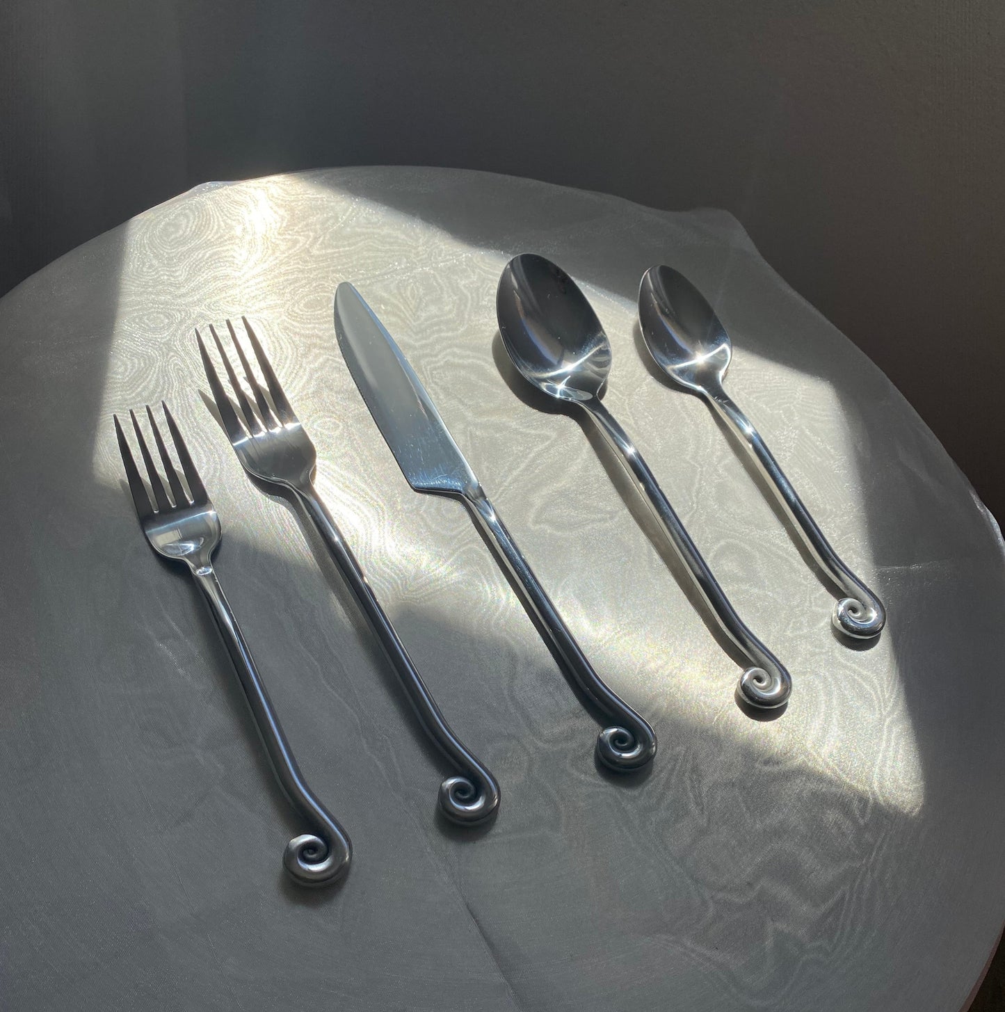 Stainless steel spiral cutlery on a chrome table  and clear tablecloth 