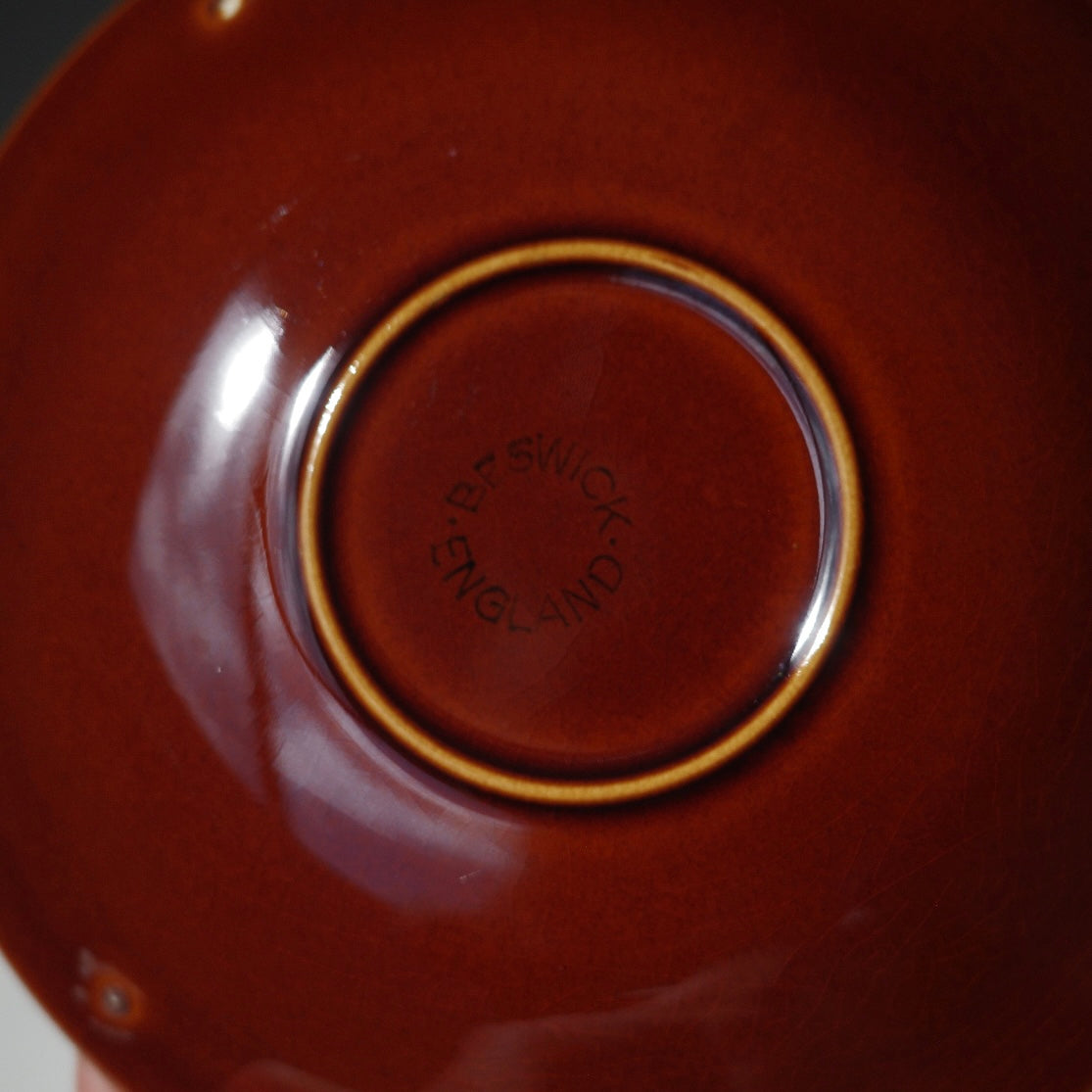 Close-up of the bottom of a glossy terracotta-colored ceramic plate or bowl