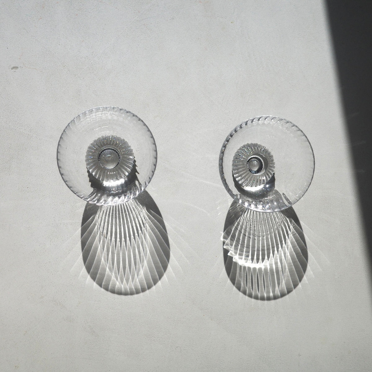 Two clear glass coupe-style cocktails glasses filled with a pale yellow liquid and each containing a small red chili pepper, photographed on a white surface with strong sunlight and shadows.